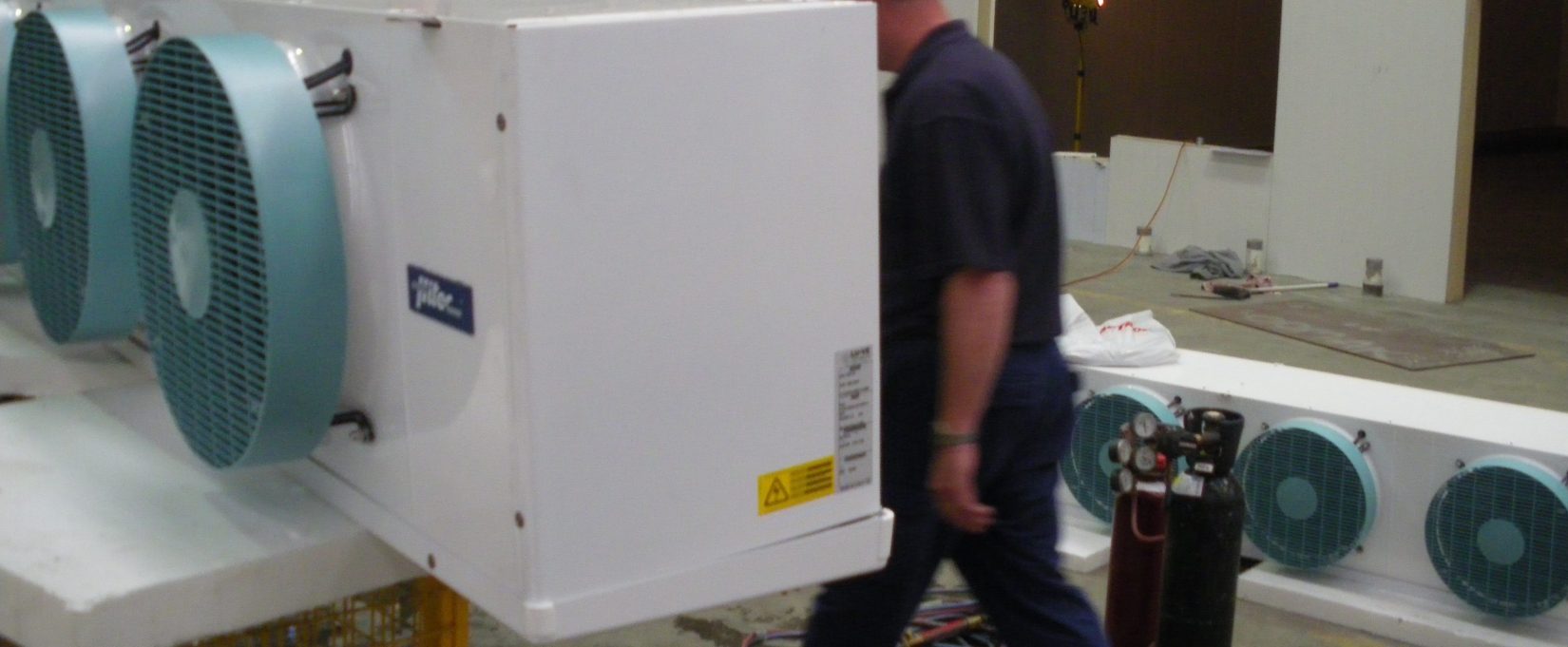 man in a blue shirt standing behind a piece of industrial refrigeration equipment