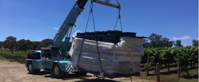 a crane carrying a refrigerated fluid chiller across a vineyard