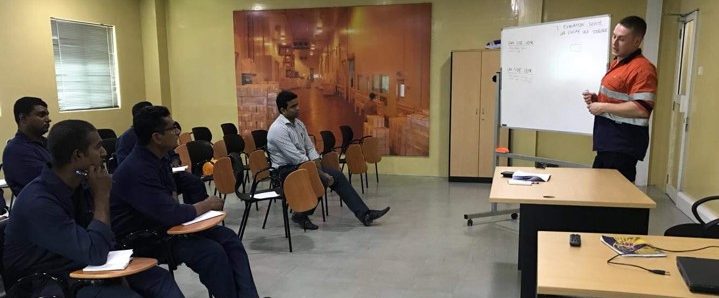 five men in a room listening to a man in front of a desk