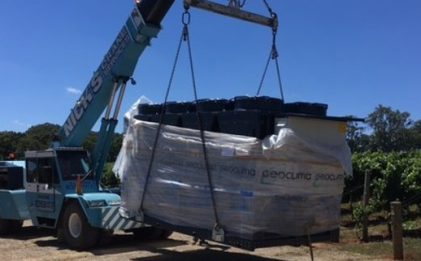 a crane carrying a refrigerated fluid chiller across a vineyard