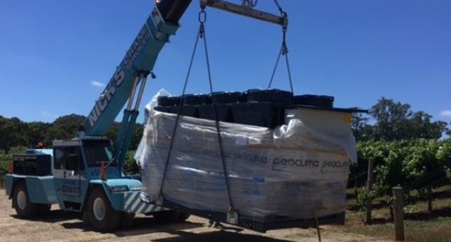 a crane carrying a refrigerated fluid chiller across a vineyard