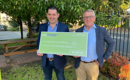 two people holding a novelty cheque outdoors in suits
