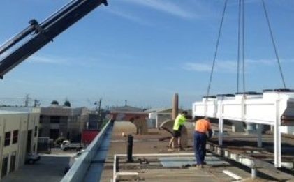 crane lowering a condenser with two men in hi vis assisting
