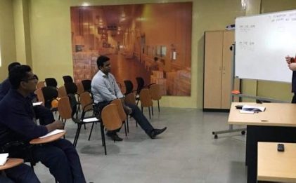 five men in a room listening to a man in front of a desk