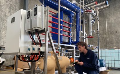 man crouching down inspecting an industrial refrigeration skid in a warehouse