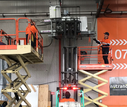 three men operating forklifts and scissor lifts to lift a piece of industrial refrigeration equipment