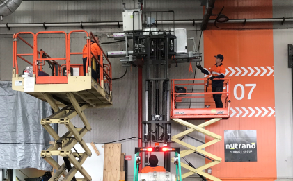 three men operating forklifts and scissor lifts to lift a piece of industrial refrigeration equipment