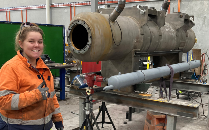 a woman in workwear standing next to an old piece of industrial refrigeration equipment in a warehouse