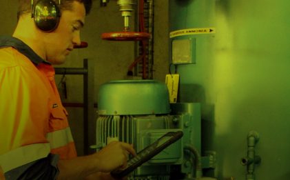 man wearing high vis workwear and hearing personal protective equipment operating a tablet while inspecting a piece of industrial refrigeration equipment