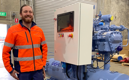 man wearing high vis workwear standing next to an industrial refrigeration compressor in a warehouse