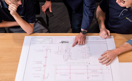 three men looking at a blueprint on a wooden table