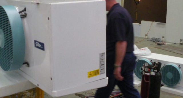 man in a blue shirt standing behind a piece of industrial refrigeration equipment